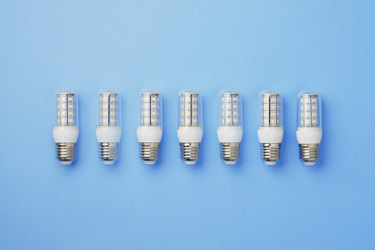 Seven LED light bulbs arranged in a row on a light blue background. Each bulb has a transparent casing with visible diodes and a white base