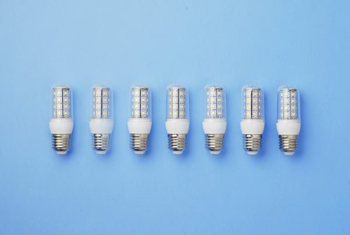 Seven LED light bulbs arranged in a row on a light blue background. Each bulb has a transparent casing with visible diodes and a white base