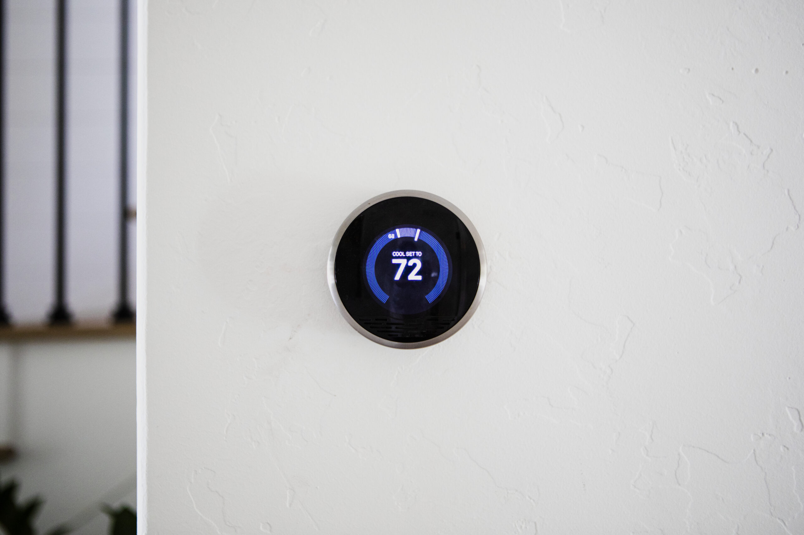 A round digital thermostat mounted on a textured white wall, displaying a temperature setting of 72 degrees Fahrenheit