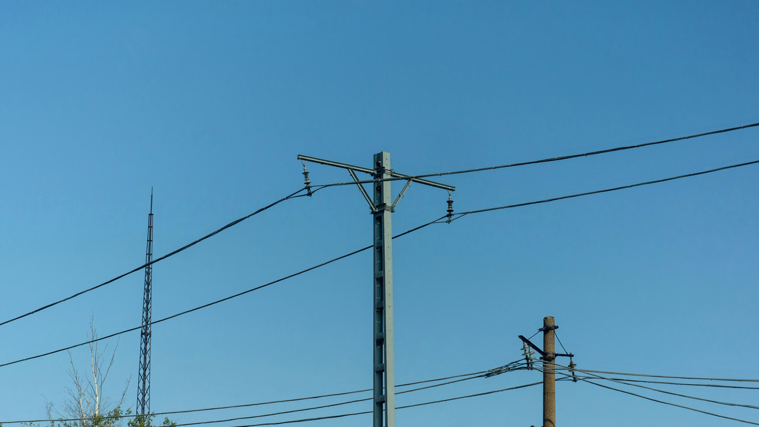A utility pole with power lines stretches against a clear blue sky. In the background, another pole and a communication tower are visible