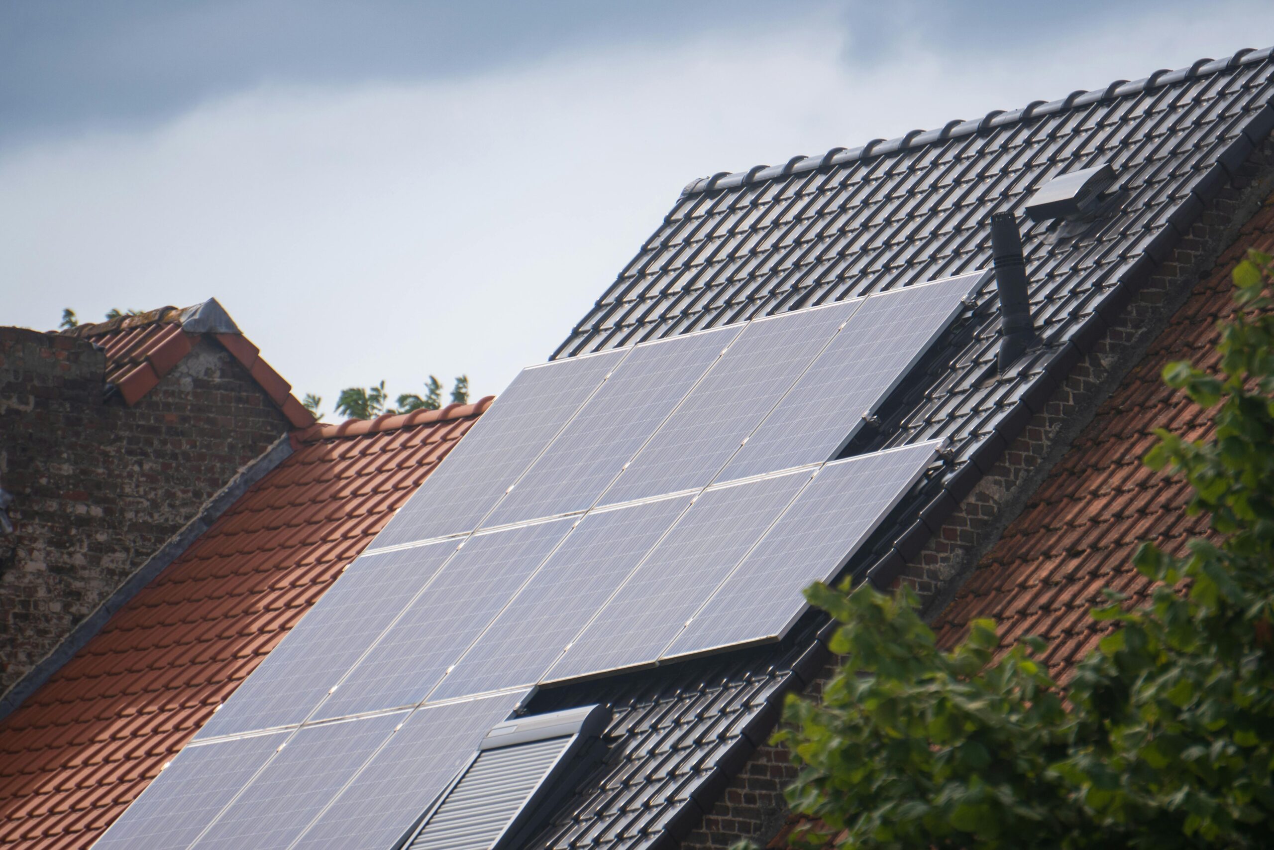 Solar panels sit on top of a residential roof. The roof is shingled and has a chimney pipe.