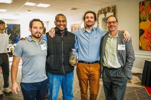 Four men stand together at a conference.